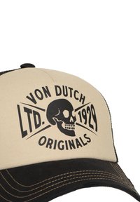 Une casquette beige et noire avec une visière noire contrastante, arborant un graphisme de crâne et le texte "VON DUTCH LTD. 1929 ORIGINALS" en noir gras.