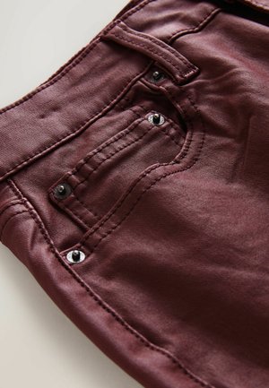 Bordeauxfarbene Denim-Jeans verfügen über eine Gesäßtasche mit schwarzen Nieten und dezenten Nähdetails. Der Stoff hat eine glatte, weiche Textur.