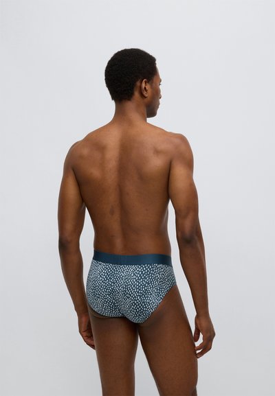 Plavky s tmavě modrým vzorem a texturovaným puntíkovaným designem. Měkký elastický pás a těsný střih, odhalující záda.