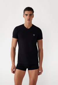 T-shirt nera a maniche corte con scollo a V, realizzata in tessuto morbido, con un piccolo logo a triangolo sul lato sinistro del petto, progettata in uno stile aderente.