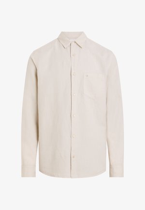 Camisa beige de manga larga hecha de tela ligera, con cuello de botón y un solo bolsillo en el pecho con bordado del logo.