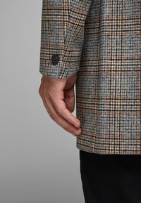 Blazer grigio in lana con un motivo a scacchi in marrone e arancione. Presenta un singolo bottone nero sul polsino e una vestibilità su misura.