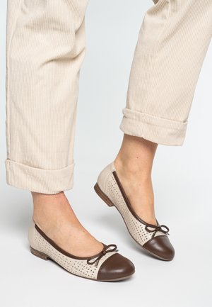 Beige leather ballet flats with brown cap toe and bow. Upper features perforated design. Paired with rolled beige corduroy pants.