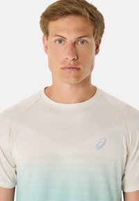 Bílý sportovní tričko s gradientem od bílé po světle modrou, texturovaným vzorem na horní části a subtilním logem na hrudi.