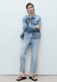 Denim jakna in lahki modri kavbojki v sproščenem kroju. Japanke z črnim trakom; gladka tekstura, klasična zasnova in subtilne podrobnosti.