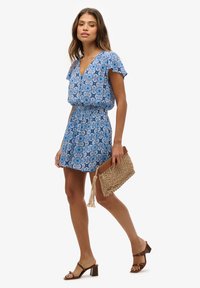 Vestido azul con estampado floral, de mangas cortas, escote en V, cintura elástica y falda acampanada. Accesorios con un bolso de mano de mimbre y sandalias marrones.