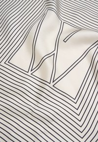 Vitt tyg med svarta linjära mönster, som har en framträdande stiliserad logotyp. Texturen verkar jämn med en lätt glans.