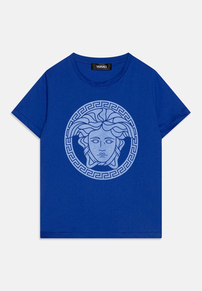 T-shirt de algodão azul com uma gráfica central de Medusa em azul claro, encerrada por um padrão circular de chave grega. Mangas curtas, gola redonda.