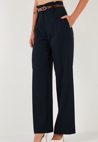 Pantaloni largi bleumarin dintr-un material neted, cu buzunare frontale și o curea din piele maro cu o cataramă din argint. Design simplu.