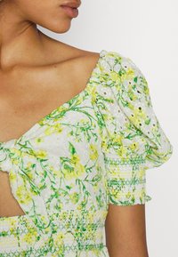 Abito floreale bianco con motivi botanici verdi e gialli, maniche a palloncino e corpetto arricciato con dettagli intricati.