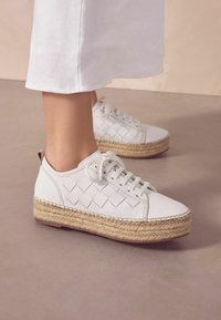 Fehér sportcipő szőtt felsőrész dizájnnal és espadrille-stílusú juta talppal. Kerek fűzőkkel és varrási részletekkel a talp szélén.