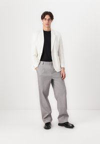 Weißes Blazer, schwarzes Hemd, graue Plisseehosen und schwarze Schuhe. Glattes Material, taillierte Passform, minimalistisches Design und klassische Farben.