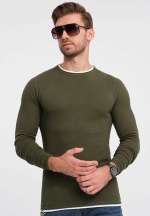 Camisa de punto verde de manga larga con una superficie texturizada y ribete blanco en el cuello, combinada con gafas de sol y un reloj.