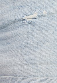 Tela de mezclilla azul claro con un detalle desgastado que presenta un desgarro, mostrando un tejido texturizado y sutiles variaciones de color.