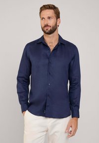 Camisa de manga larga azul marino en tejido ligero. Presenta un cuello clásico, cierre de botones y un ajuste ceñido. Textura suave y diseño ajustado.