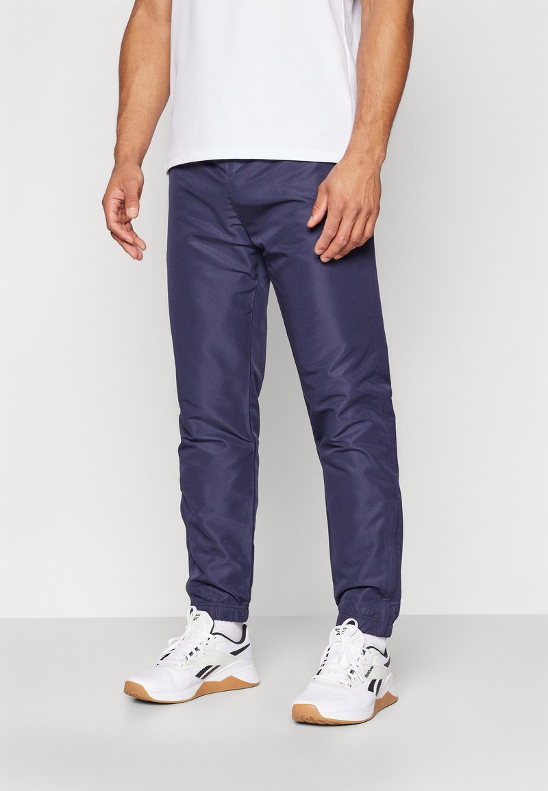 Joggeurs légers bleu marine avec des poignets et une taille élastiques. Texture lisse avec des poches latérales. Portés avec des baskets blanches et un T-shirt uni.