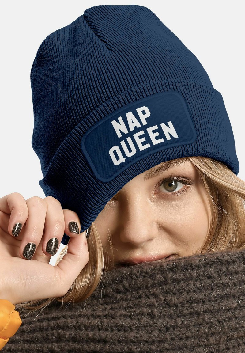 Navy blue knit beanie with a rectangular patch featuring white text that reads "NAP QUEEN." Textured fabric and snug fit.