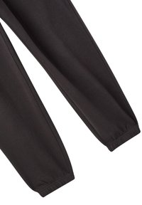 Černé joggingové kalhoty s elastickými manžetami, které ukazují texturu tkaniny a švy na bílém pozadí.