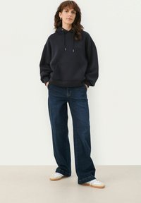 Marininspirerad oversize hoodie med sidofickor, i kombination med vida mörk denimjeans. Looken kompletteras av vita sneakers med gummisula.