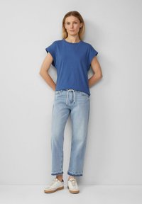 Blaues T-Shirt mit kurzen Ärmeln und lässiger Passform, kombiniert mit hellblauen, geraden Jeans und beigen Sneakern mit strukturierten Akzenten.