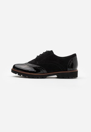 Zwarte brogueschoen met glanzende neus en hiel, suède middenstuk, veters aan de voorkant en dikke, robuuste zool met bruine rand.