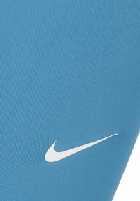Leggings Nike de color azul claro, fabricados con tejido acanalado, que presentan un logo Swoosh blanco. El diseño enfatiza una forma ajustada y una textura suave.