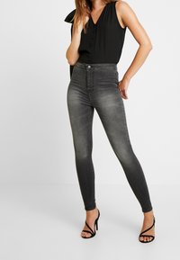 Szare, wysoki w pasie dżinsy skinny z przetarciami, z zapięciem na guzik i zamek. Połączone z ciemną, bezrękawnikową bluzką i czarnymi szpilkami.