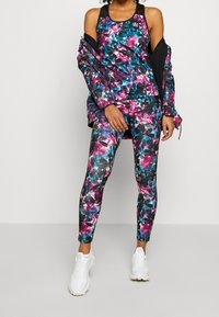 Conjunto deportivo que incluye una camiseta sin mangas de colores y leggings estampados en negro, rosa y azul. Incluye una chaqueta con acentos texturizados.
