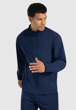 Giacca navy blue con zip, realizzata in tessuto testurizzato, caratterizzata da un colletto alto e due tasche laterali, completata da polsini aderenti.