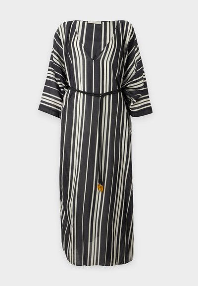 Robe à rayures verticales noires et blanches avec col en V, manches trois-quarts amples et fine ceinture noire avec petits pompons à la taille.