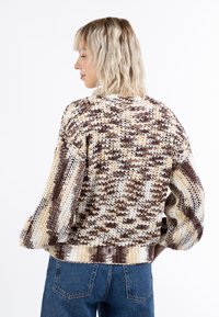 Šviesiai kreminė, ruda ir rusva megzta megztinis su stambiu audiniu, per dideliu siluetu ir raukšlėtu kraštu. Savybė – laisvos balioninės rankovės dizainas.