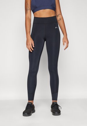 Navy korkeavyötäröiset legginsit joustavasta kankaasta, kontrastisaumoilla, slim fit -muotoilu ja logotaito vyötärön lähellä. Yhdistetty mustiin lenkkitossuihin.