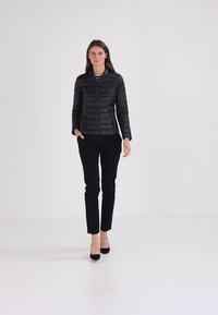 Crna puf jakna s horizontalnim šavovima, visokim ovratnikom i zatvaranjem na zip, uparena s crnim uskim hlačama i crnim visokim potpeticama.