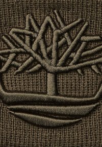 Logo di un albero ricamato con fili verde scuro su uno sfondo in maglia marrone testurizzata. Presenta un design intricato di rami e radici.