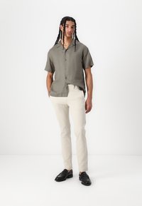 Camicia in lino verde oliva a maniche corte con colletto, abbinata a pantaloni aderenti color crema e mocassini neri.