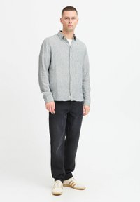 Light gray striped button-up shirt with a chest pocket, paired with dark denim trousers and cream sneakers with brown stripes.