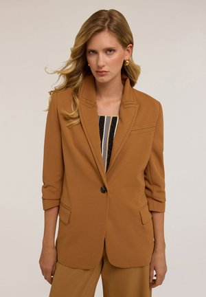 Blazer marron ajusté avec un col à revers, fermeture à un bouton, deux poches avant et manches retroussées. Tissu lisse avec un subtil détail de couture.