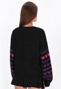 Svart tröja med en texturerad yta, prydd med färgglada hjärtmönster i rosa och lila på ärmarna. Rund halsringning och avslappnad passform.
