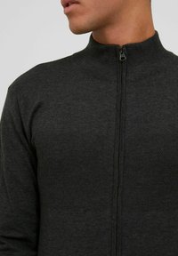 Mörkgrå stickad zip-up-tröja med hög krage, texturerat övre panel och slätt nedre parti. Har en central dragkedja.