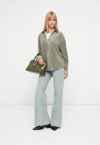 Oliwkowa kordrowa koszula na guziki, jasnoniebieskie szerokie spodnie, oraz błyszcząca zielona torebka ze srebrnymi akcesoriami, zestawione z czarnymi butami.