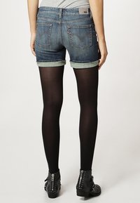 Denim shorts with rolled cuffs, dark blue wash, two back pockets; paired with black opaque tights and studded black ankle boots.