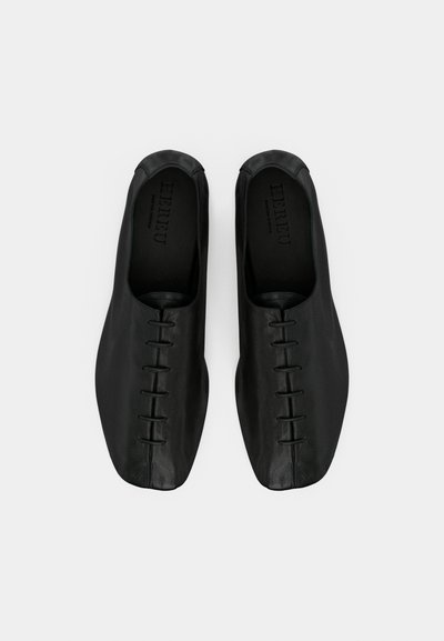 Μαύρα δερμάτινα παπούτσια χωρίς κορδόνια με λεία υφή, που διαθέτουν μοναδικό ραμμένο σχέδιο στο επάνω μέρος και στρογγυλεμένη μύτη.