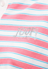 Ύφασμα με ριγέ μοτίβο σε ροζ, λευκό και μπλε χρώμα με ασημένια γκλίτερ κεντημένο κείμενο "JOOP! JEANS" και λευκό κουμπί.