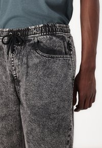 Black and gray marbled sweatpants with an elastic waistband, drawstring closure, and side pocket detail. Fabric appears soft with subtle texture.