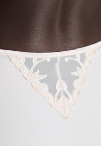 Hvit undertøy med en gjennomsiktig, blonderpanel bak, prydet med et blomsterdesign i pastellrosa og bølgete kanter. Myk tekstur.