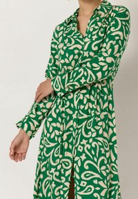 Vihreä kuviollinen mekko pitkillä hihoilla, jossa on off-white kukkakuosi. Sisältää kauluksen ja nappisuljin etuosan.