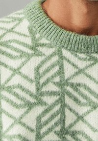 Pull vert et blanc à motif avec un design géométrique de feuilles, en matière tricotée douce, avec un col côtelé.