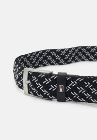 Cintura elastiche intrecciate nera con motivo diagonale bianco. Caratterizzata da una fibbia in metallo argentato e un accento nero con dettagli del logo.