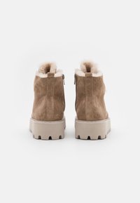 Bottines en suede marron avec une finition texturée, doublure en fausse fourrure, fermeture éclair, et une épaisse semelle en caoutchouc beige avec un relief.