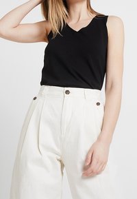 Black sleeveless top with a v-neckline and relaxed fit paired with high-waisted white wide-leg trousers featuring two front buttons.